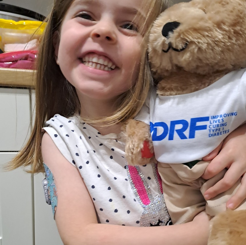 Alys wearing her Dexcom glucose sensor with her Breakthrough T1D UK teddy bear, Rufus.