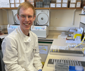 A researcher sits in a lab beside screening samples and lab equipment for early detection of type 1 diabetes.