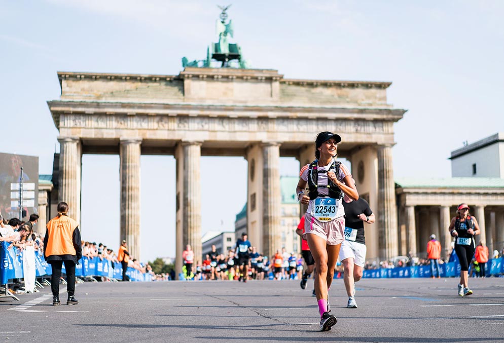 Smiling female runner in Berlin Marathon with crowds lining road.