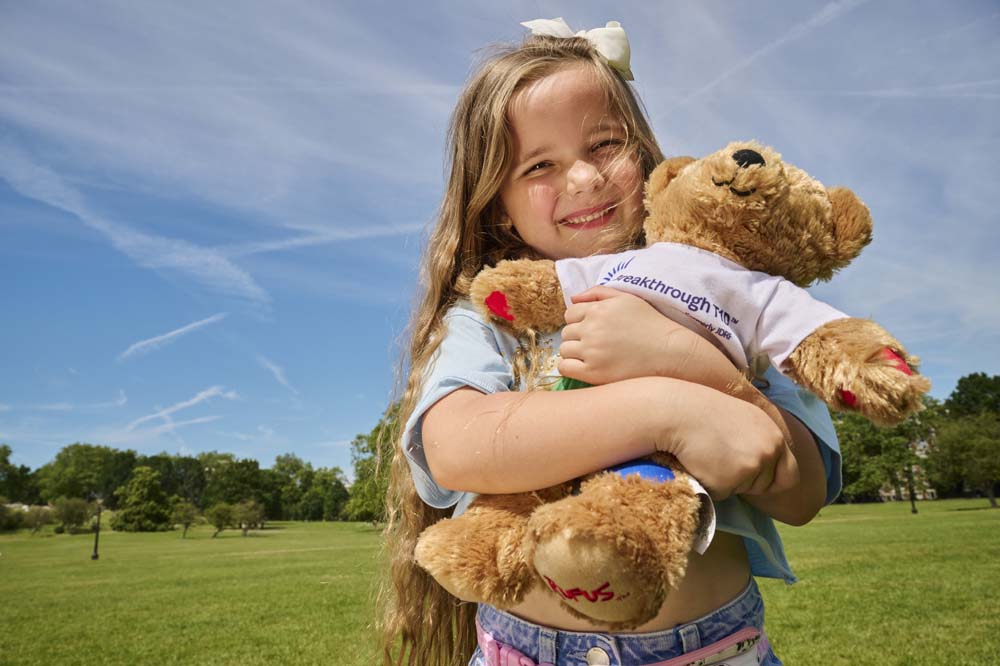 Smiling girl holding Breakthrough T1D Rufus bear in park