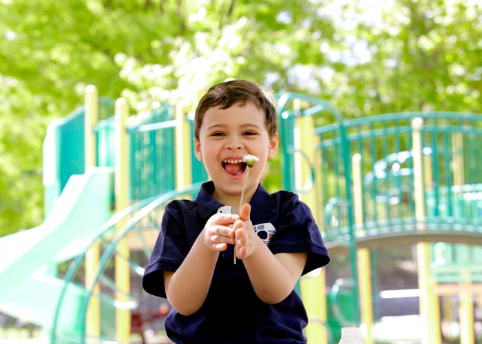 Smiling boy in playground holding a flower to face