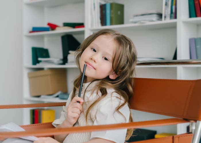 Young girl sat in chair with pencil resting on chin