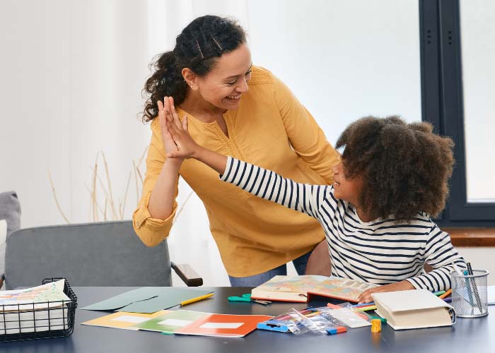 Adult high-fiving a child at a desk in school