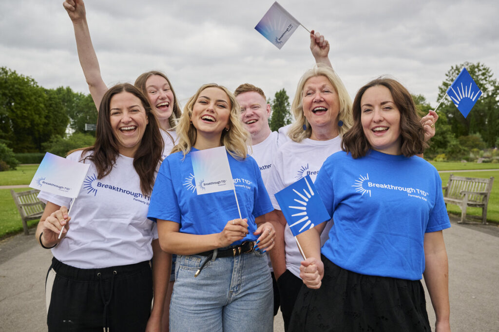 A group of people wearing Breakthrough T1D t-shirts are cheering and waving flags.