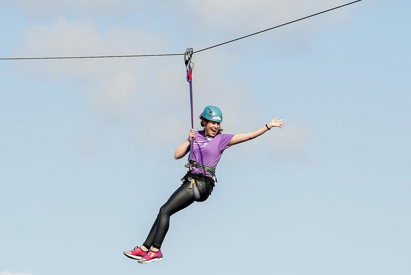 Waving woman doing Glasgow Clyde Zipline hanging from wire over River Clyde in Scotland