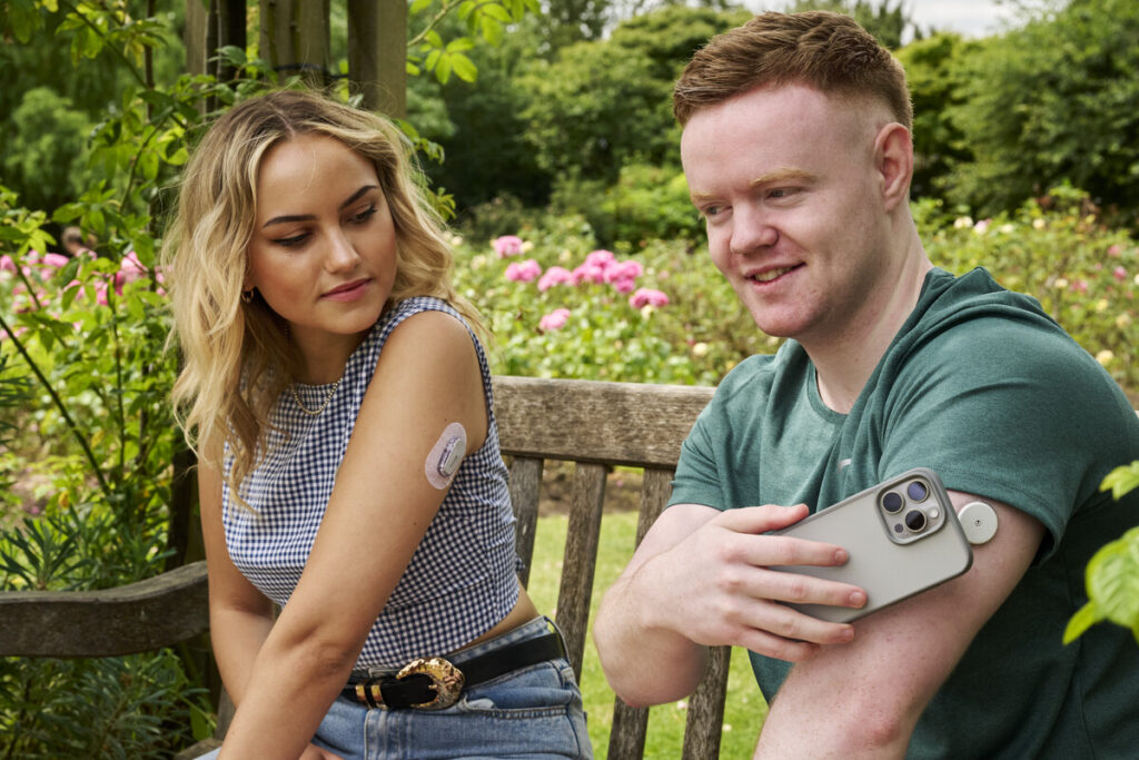 female and male sat on bench both wearing diabetes sensors