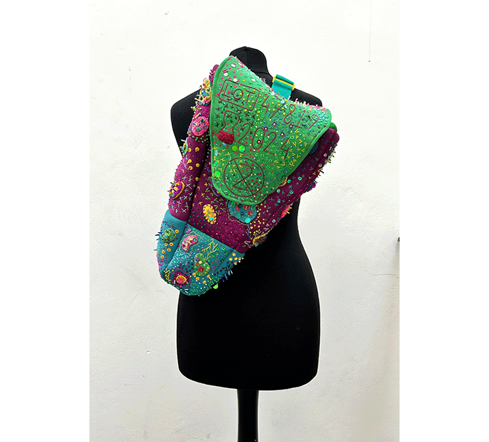 Megan Neville's brightly coloured, bold day handbag sculpture with detailed embroidery on a limbless mannequin using a cross-body strap. Designed for her project Ordinary Oddness.