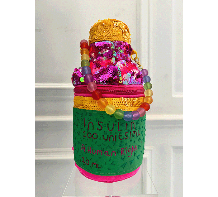 Megan Neville's Evening Bag for her project, Ordinary Oddness. Bold and brightly coloured, it's designed in the shape of an insulin vial. It has a bold pink zip, A beaded handle, pink sequin detail. The bag features the text: Insulin 100 units/ML. A Human Right. 10 ML.