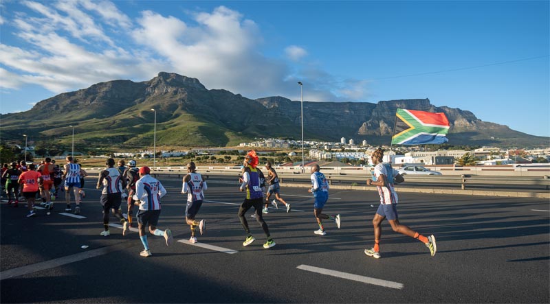 Cape Town Marathon runners from behind on a road with mountains in the background.