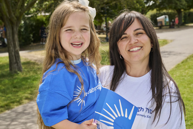 A woman holds a young child, and they are smiling at the camera.
