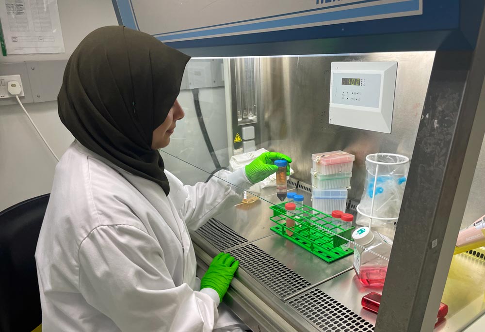 Female researcher holding a vial in gloved hand.