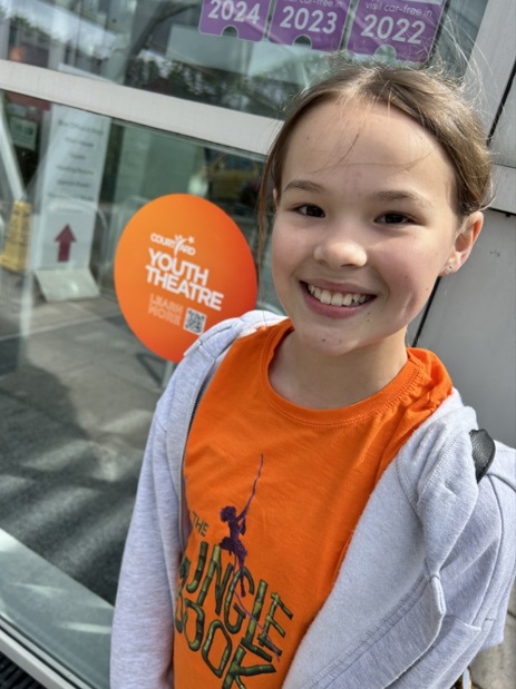 Image of young girl in orange t-shirt smiling at camera