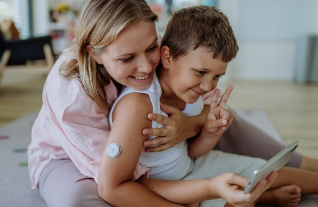 Mother with blonde hair and son with brown hair smiling and hugging taking photograph on smart phone.