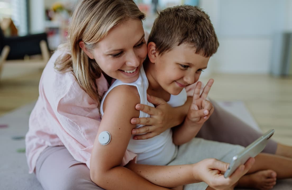 Mother with blonde hair and son with brown hair smiling and hugging taking photograph on smart phone. 