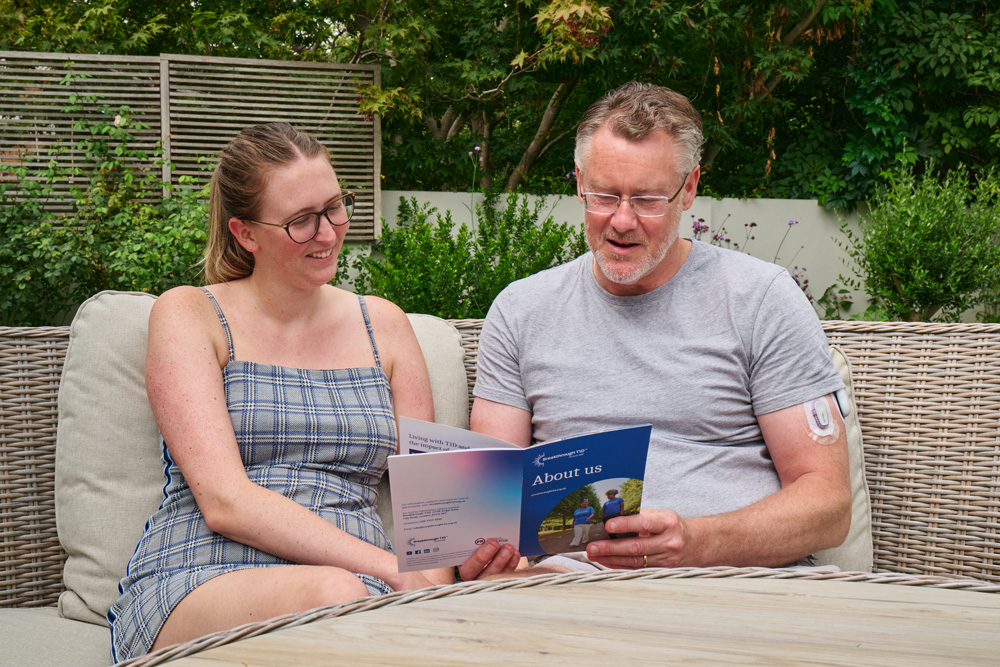 Andy reading Breakthrough T1D type 1 diabetes information leaflet at a table in the garden.