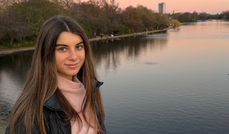 A young woman standing in front of a river looking directly into the camera.