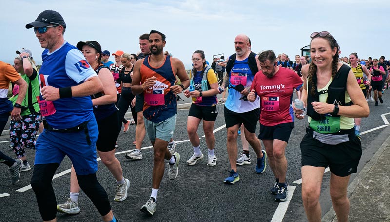 Large mixed group of racers running in a marathon in a road under grey sky.