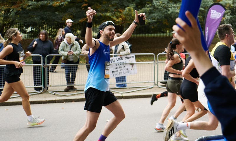 Man running in marathon in London park with his arms up in celebration
