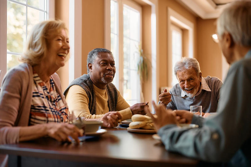 Four people around a table laughing as they eat a meal.
