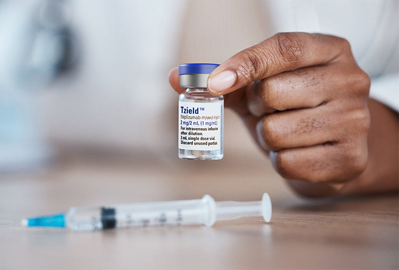 Close up of a doctor's hand holding an injection vial of Tzield teplizumab near a syringe