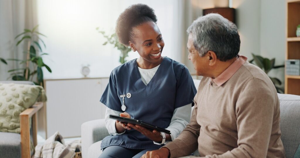 Smiling female nurse with older man in lounge, holding a tablet device