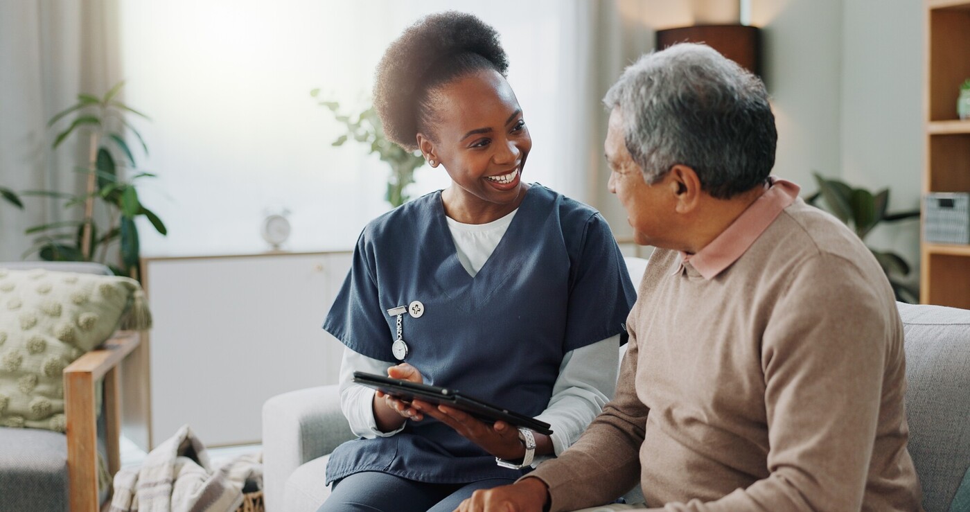 Smiling female nurse with older man in lounge, holding a tablet device