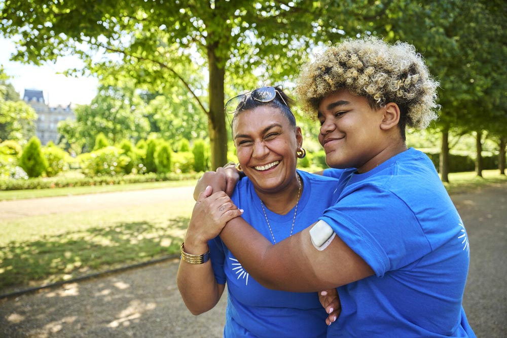 Woman and young man outside in the park smiling, wearing T-shirts to represent Breakthrough T1D, a funder of type 1 diabetes research. Insulet Omnipod pump visible on one arm.