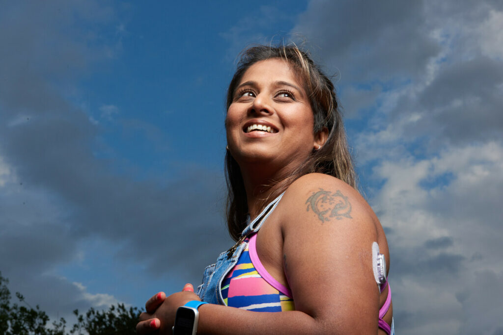 Smiling woman wearing a Dexcom G6 CGM (continuous glocose monitor) sensor.